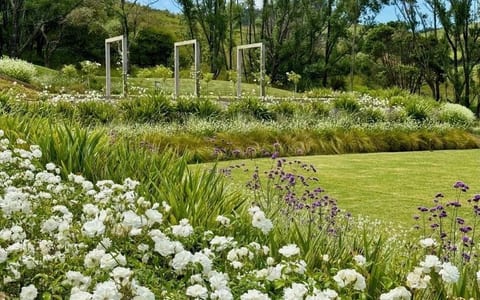 Landscaped gardens with white flower borders, ornamental grasses and timber arch frames on a lawn