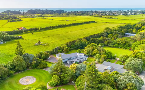 Aerial view of house and grounds surrounded by trees and farmland with coast in background