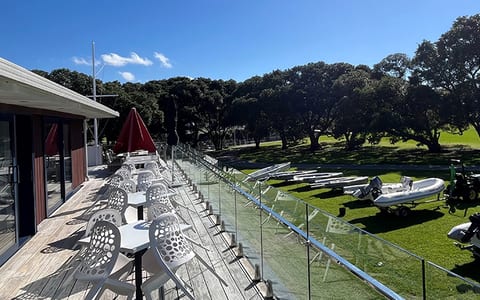 Outdoor deck with white chairs and tables overlooking lawn and boats