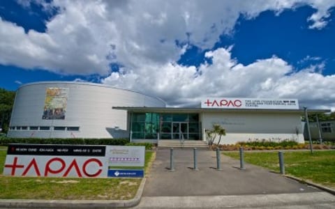 Performing arts centre exterior with cylindrical curved facade and centre signage under blue sky