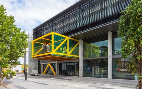 Contemporary building with yellow steel canopy box, concrete pillars, and glazed facade, urban setting