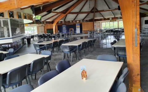 Large club room with circular timber ceiling, long tables and chairs, and a small raised platform at the far end