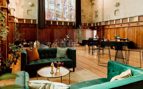 Historic hall interior with dark timber panelling, stained glass windows and lounge seating
