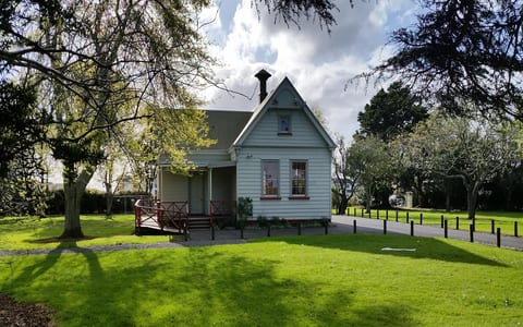 Small heritage villa-style hall with verandah set on a lawn surrounded by trees