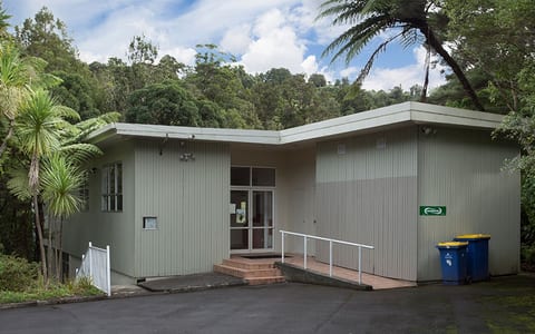 Single-storey community hall with vertical cladding and access ramp surrounded by trees