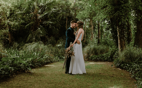 Two people embracing in a dense garden clearing surrounded by trees and lush planting