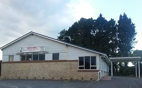 Single-storey white-painted brick community hall with low-pitched roof and car park, trees behind