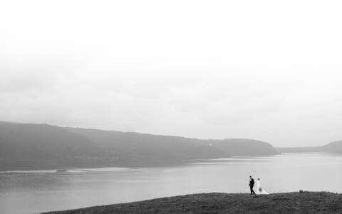 Two figures on grassy hillside beside a lake with misty hills, black and white landscape