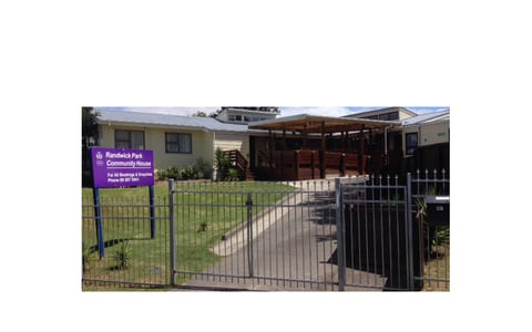 Single-storey community house behind iron fence with signage and covered deck