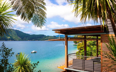 Waterfront timber lodge building with a deck and jetty, surrounded by native bush and a sheltered cove