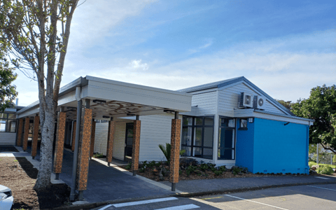 White weatherboard building with a covered canopy entrance featuring patterned carved posts