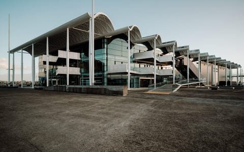 Large steel and glass event centre exterior with curved roof canopy and open forecourt