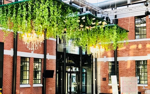 Industrial brick atrium interior with hanging greenery, chandeliers, and dark polished floor