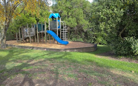 Playground structure with slide surrounded by wood chip and lawn, set among trees