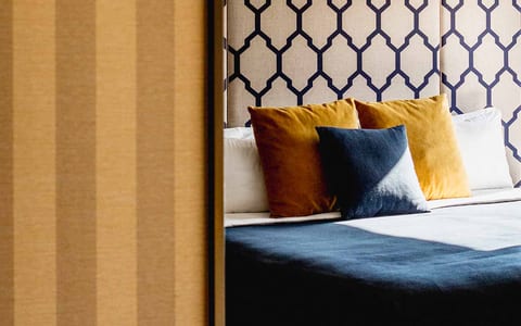 Hotel bed with patterned headboard and ochre cushions