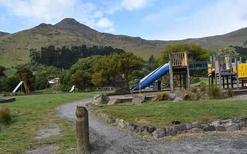 Park with playground equipment, trees, and hill backdrop
