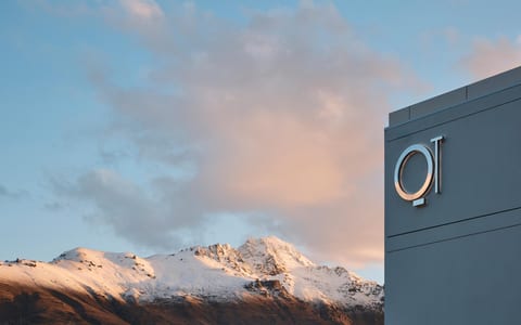Grey rendered building exterior with brand signage, snow-capped mountains behind