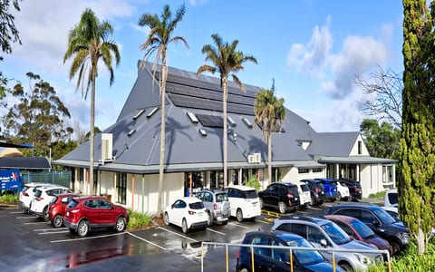 Community centre building with distinctive peaked roof and palm trees, car park in foreground