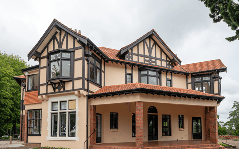 Two-storey cream and red-brick Tudor-revival homestead with terracotta tile roof, covered entrance porch