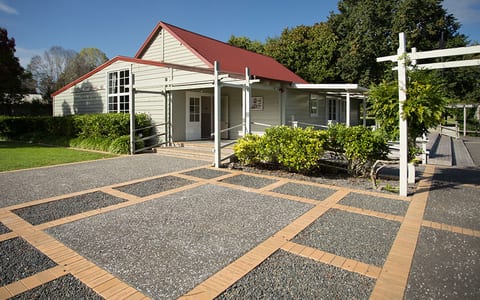 White weatherboard hall with red roof, covered veranda, and gravel forecourt