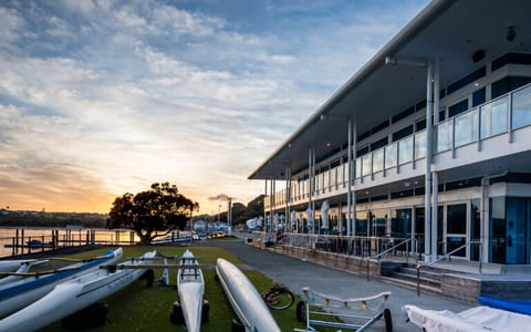 Two-storey waterfront function centre at sunset with boats on the foreshore