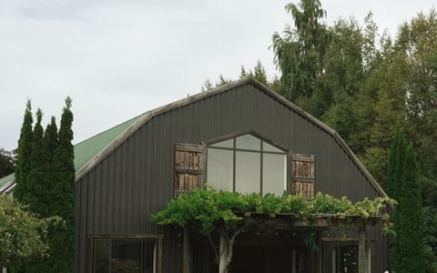 Dark-clad barn venue building viewed across lawn with cypress trees flanking the entrance and wine barrels at the porch