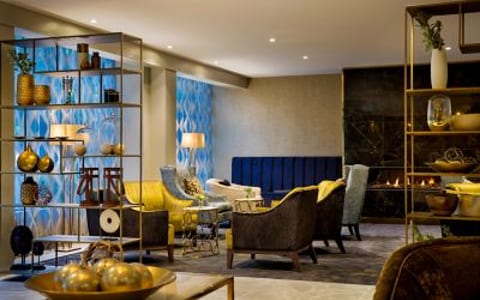 Hotel lounge with yellow and brown armchairs, open shelving with decorative objects, blue patterned wall panels