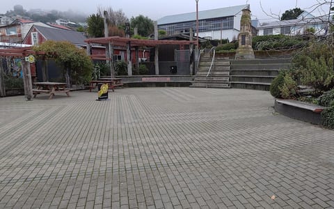 Open paved town square with seating, pergola structures, and memorial column