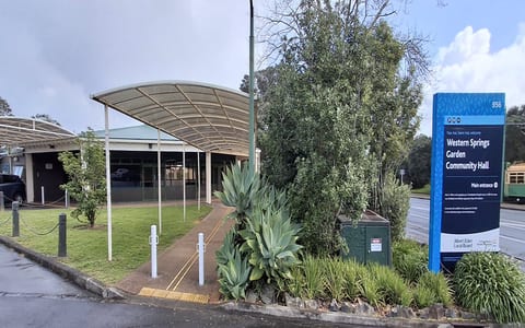 Low-rise hall with curved canopy entrance, sign post, and planted border, roadside setting