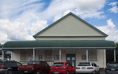 Weatherboard hall building with green roof and cars parked in front