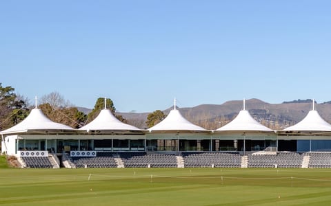 Cricket oval grandstand with distinctive peaked white canopy roofs and hills behind
