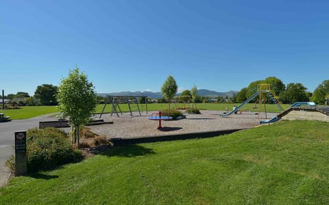 Open park with playground equipment, trees and mountain backdrop