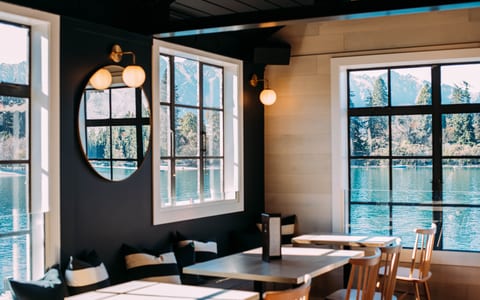 Dark-painted interior with black ceiling beams, round mirror, globe wall lights, and lake and mountain view through white-framed windows