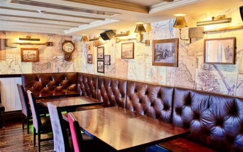Bar interior with dark timber banquette seating, tufted leather backs, map-print wallpaper, and wall sconce lighting