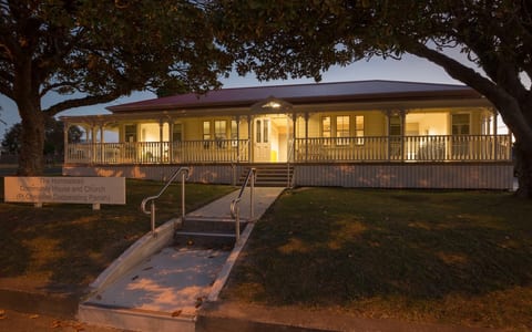 Illuminated heritage villa-style building at dusk with verandah and signage, trees framing