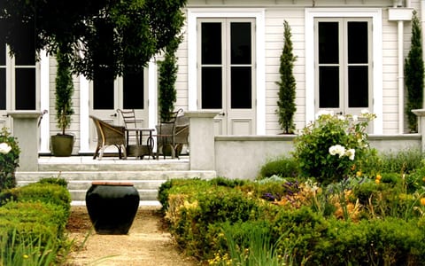 White heritage homestead with a formal parterre garden, columnar cypress trees and rose borders