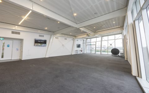Large open hall with carpeted floor, angled ceiling and glazed wall