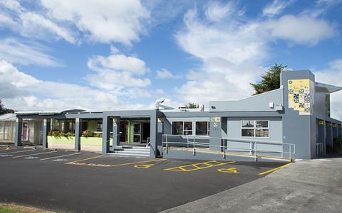 Single-storey blue community centre building with mural on fence, car park in front