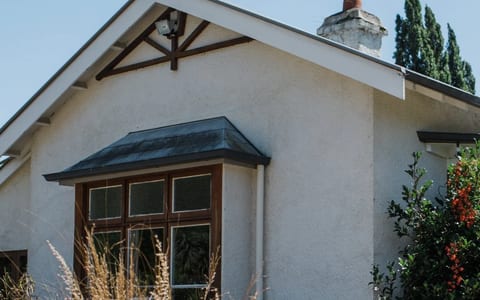 White rendered cottage exterior with chimney, ornamental grasses and shrubs in the foreground