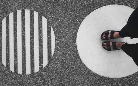 Overhead view of feet in sandals standing on painted circle markings on asphalt