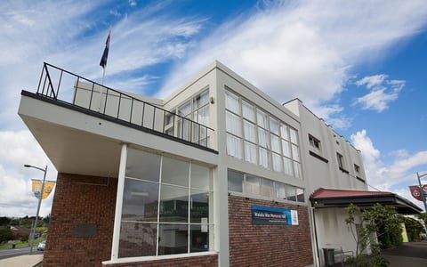 Two-storey cream and brick hall with rooftop balcony, large windows, and flagpole