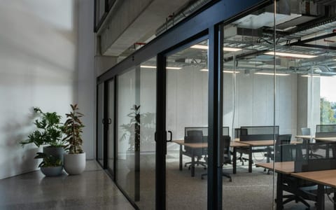 Glass-partitioned office space with hot-desks and plants in a polished concrete corridor