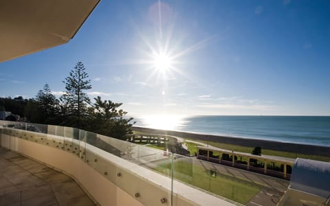 White rendered building balcony with glass balustrade overlooking beach, sea and pine trees