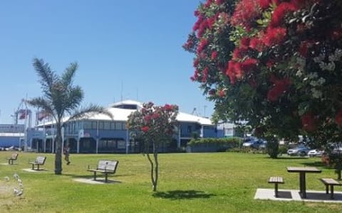 Club building exterior viewed from waterfront with lawn and trees