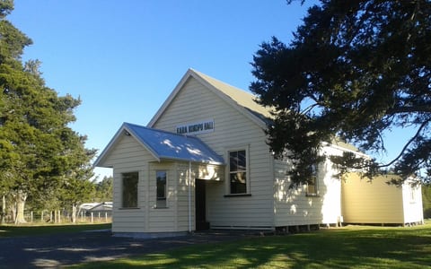 Small white timber hall with metal roof and signage on grassed section