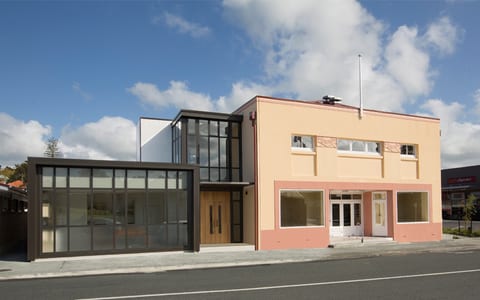 Salmon-rendered two-storey hall with glass extension and dark-framed shopfront, street view