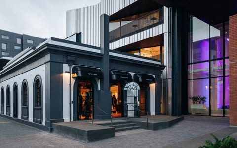 Dark rendered heritage building with arched shopfront openings and modern upper addition, street entrance at dusk