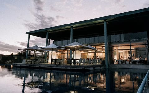 Winery building at dusk reflected in an infinity pool with lit terrace umbrellas