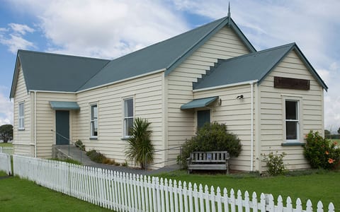 Cream weatherboard hall with teal roof and picket fence in open rural setting