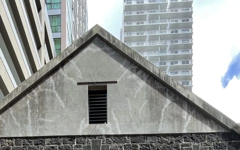 Dark basalt stone warehouse exterior with arched entry and gabled roofline, flanked by city towers